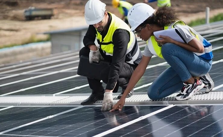 Two engineers in high vis jackets knelt down examining solar panels on a solar farm