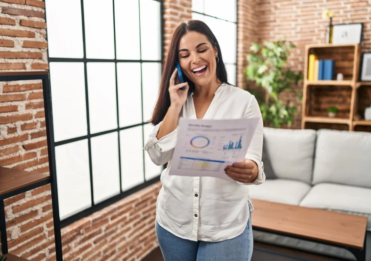 woman smiling while looking at an energy bill and speaking on the phone