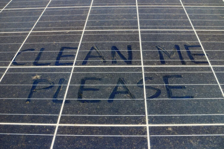 a dirty solar panel with "clean me please" written on it