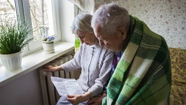 elderly couple huddled by radiator looking at energy bill