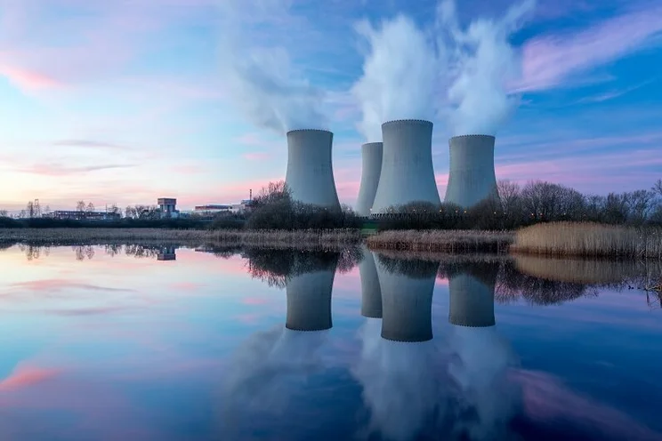 Nuclear reactor at dusk, with four cooling towers ejecting steam into the air above