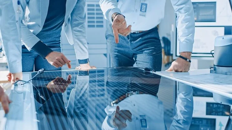 Solar panel on lab table with engineer in white shirt with office tags pointing at it