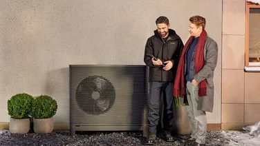 Installer and male customer looking at at phone app in front of Aira heat pump outdoor unit