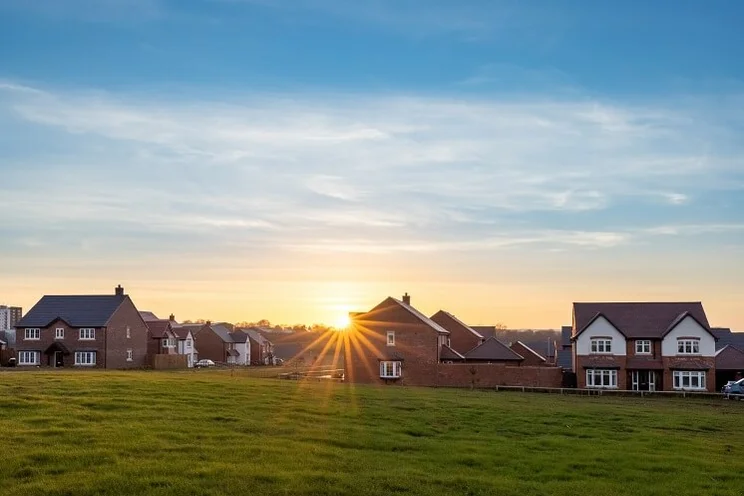 sun setting behind houses in a housing estate with a green field in the foreground