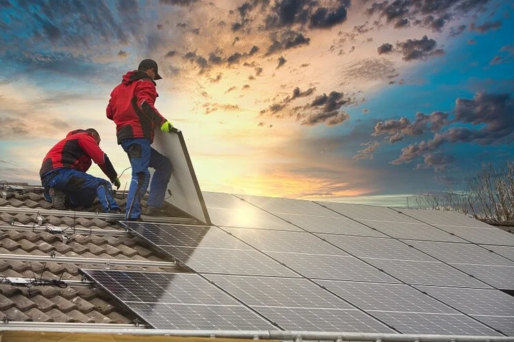 Two people installing solar panels on a roof with a sunset in the background