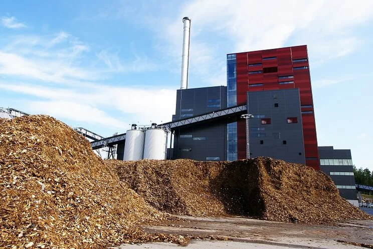 Piles of wood chips outside a red and grey biomass energy plant