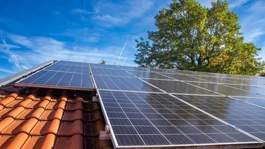 solar panels on red tile roof with blue sky and tree in background