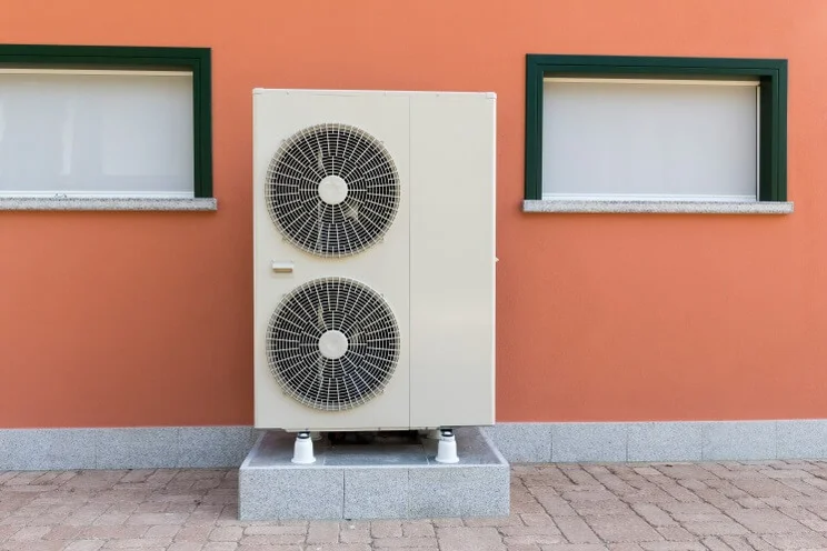 air source heat pump on a wall outside an orange house