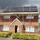 red brick detached house with scaffolding around it and solar panels on roof, dark clouds in background
