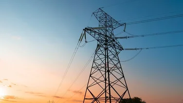An electricity pylon at dusk, with wires running to another pylon in the distance.