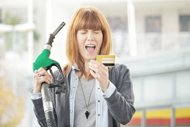 Woman holding petrol pump looking anguished and holding a credit card