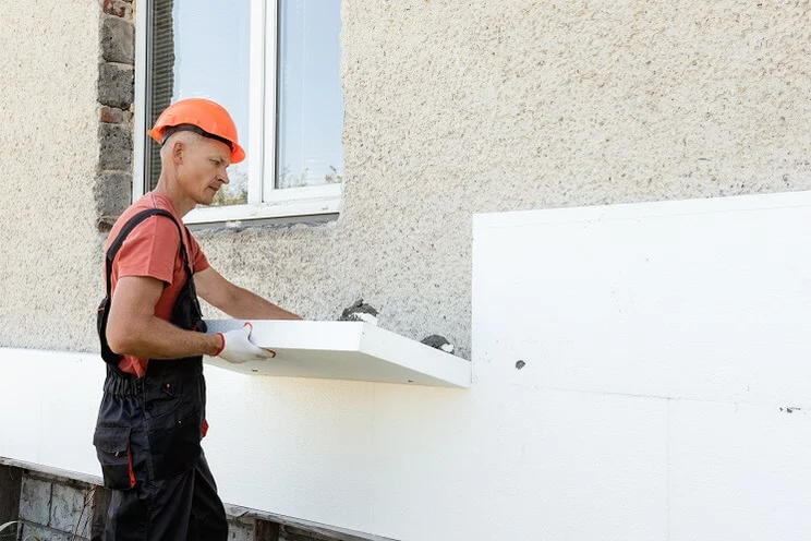 Contractor installing external wall insulation on outside of house