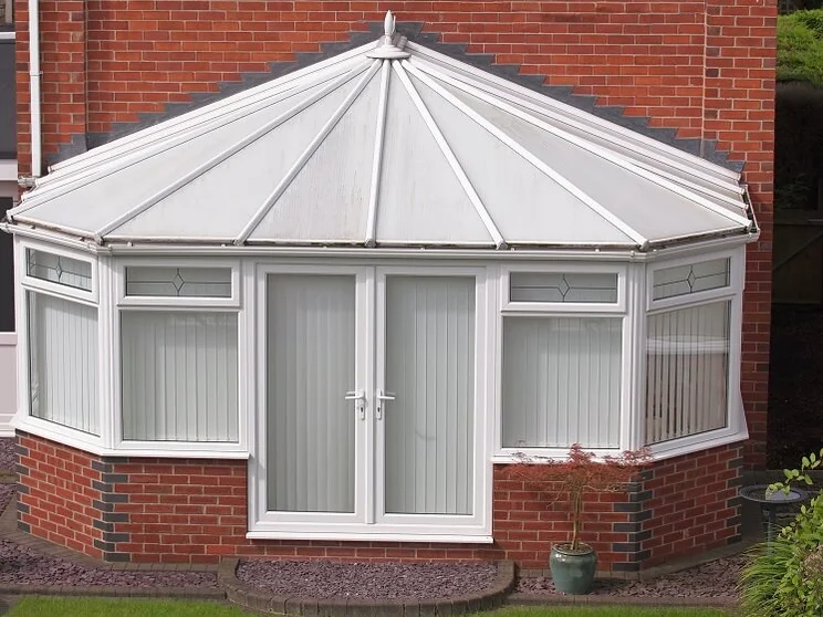 outside of conservatory with white paneled roof, brick dwarf wall, and blinds on inside