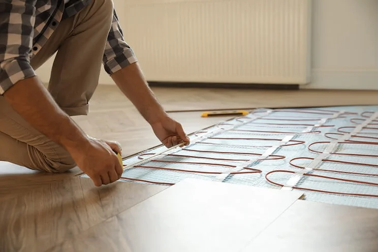 man installing electric underfloor heating cables under wooden floorboards