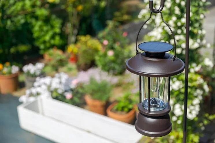solar-powered lantern hanging from metal pergola in flowery garden