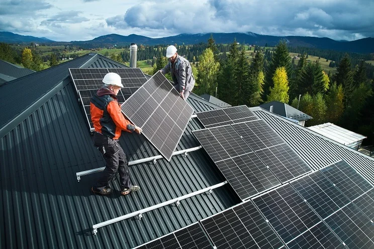 Two installers carrying a black solar panel onto a roof
