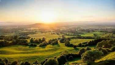 sunset over green fields and trees seen from a hill