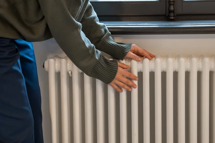Woman warming hands on white radiator at home
