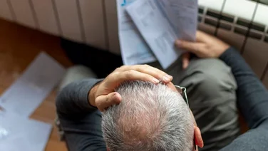 Top down view of man looking at high energy bills with his hand on his hand, looking stressed