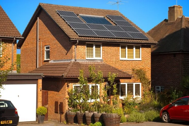solar panels on roof of red brick house with trees and red car parked in driveway