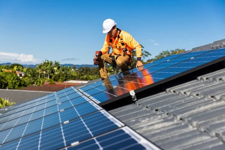 Solar panel technician in orange with drill installing solar panels on a roof