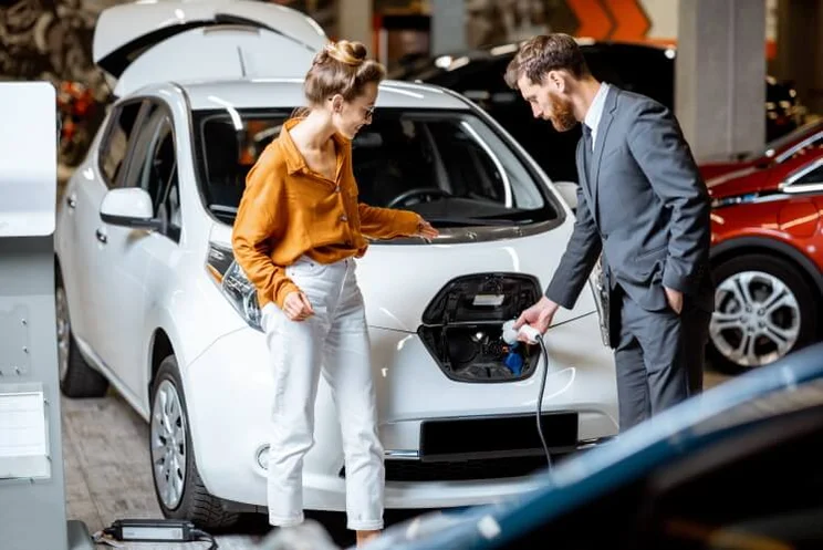 Sales manager with client near electric car at a car dealership