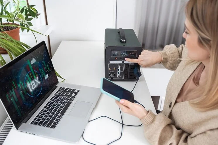 Woman charging phone and laptop at home with portable solar battery
