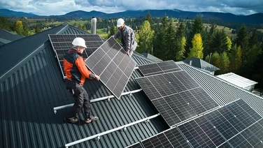 Two installers carrying a black solar panel onto a roof