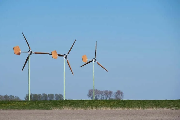 three small wind turbines in a field with trees in distance