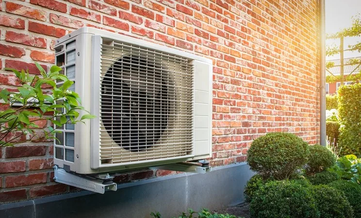 Heat pump outside a home against a red brick wall
