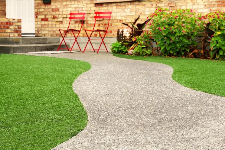 Garden with two red chairs and a grey wiggly pathway bordered by green artificial grass