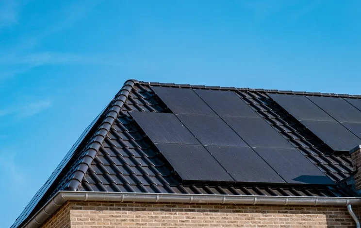 black solar panels on a dark roof under a blue sky