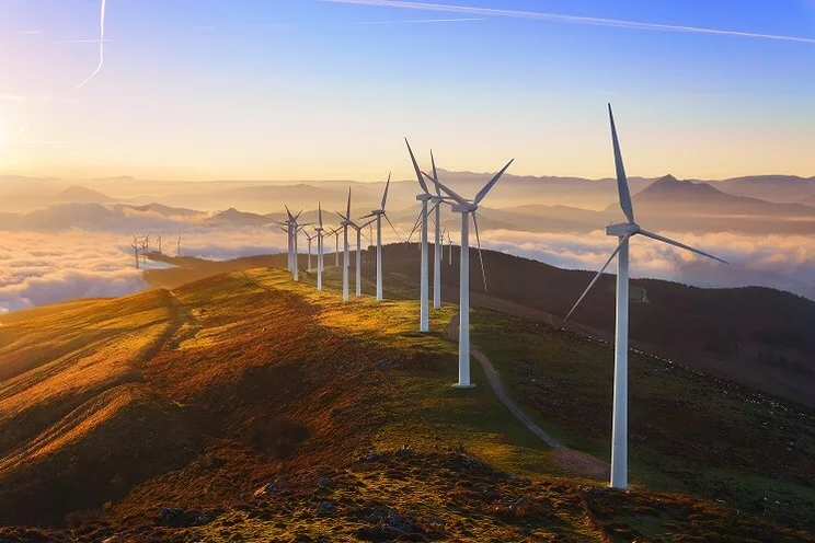 A group of wind turbines perched on top of a hill at sunset
