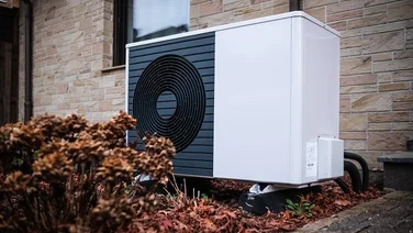 Air source heat pump unit outside a home surrounded by autumn leaves