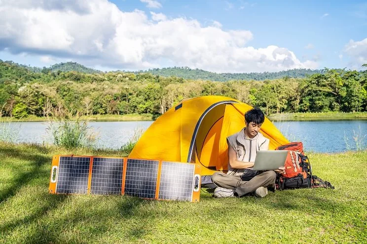 Young man camping and charging laptop with using portable solar panel