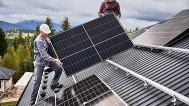 People installers carrying a solar panel on a roof with a cloudy sky in the background