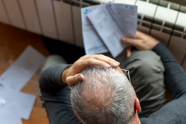Top down view of man looking at high energy bills with his hand on his hand, looking stressed