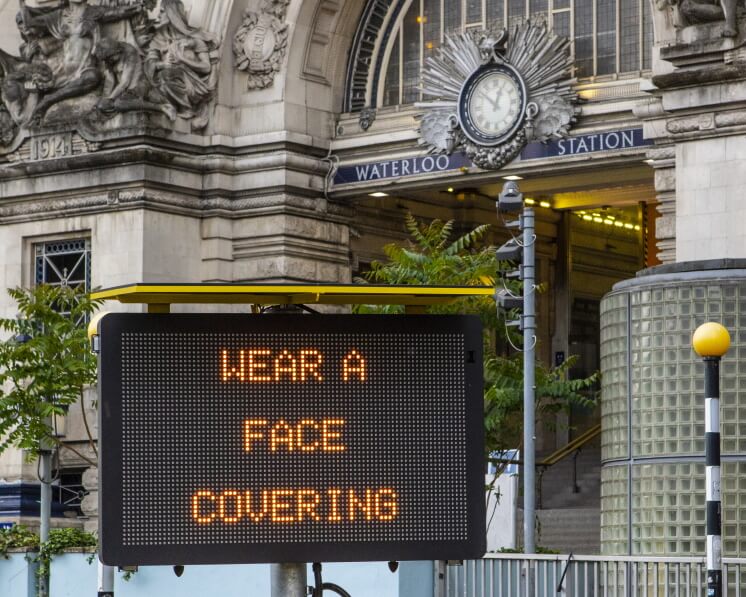 a COVID-19 sign outside Waterloo Station, reading "wear a face covering"