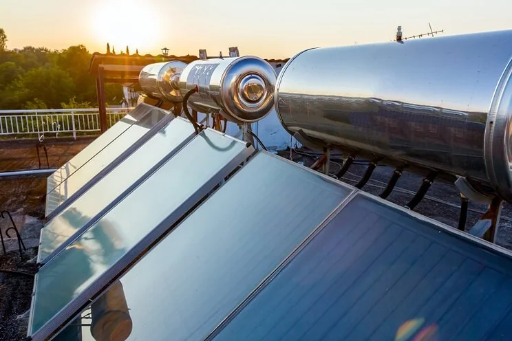 six solar thermal flat plate panels mounted on a flat roof with sun setting in background