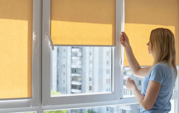 woman pulling down yellow blinds over a window to keep the sun out of a room