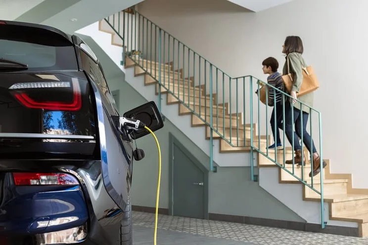 Electric car charging in a family home as a parent and her child walk upstairs
