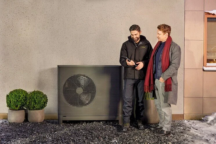 Installer and male customer looking at at phone app in front of Aira heat pump outdoor unit