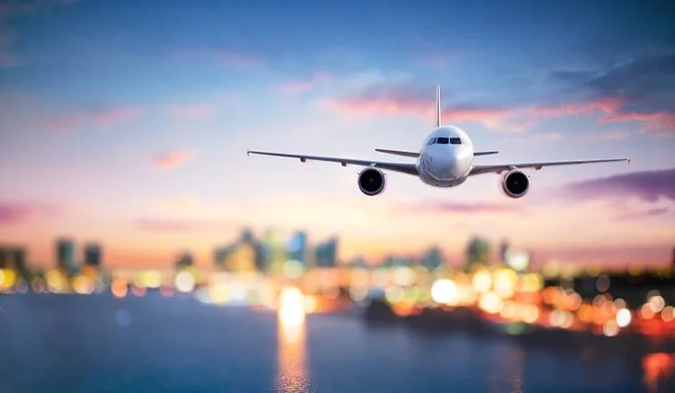 aeroplane landing on airport runway at dusk with blurred city lights in background