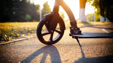close up of front wheel of an electric scooter on road with sun setting in background