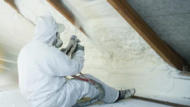 Man in protective gear applying spray foam insulation to roof
