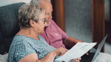 Side view of elderly couple at home paying bills online via laptop