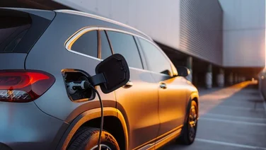 dark grey electric car plugged in to charge with grey office building in background
