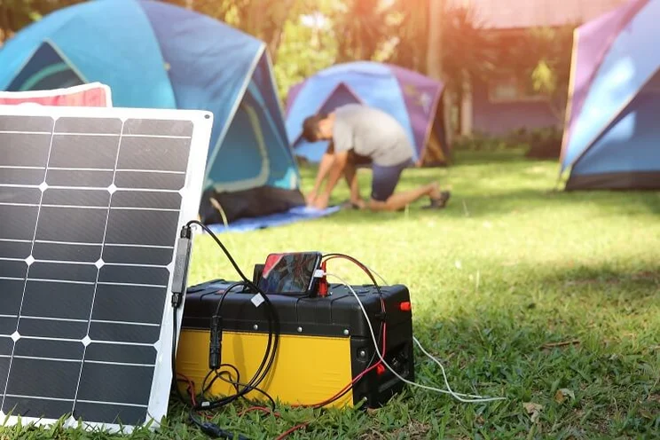portable solar generator connected to solar panels with man setting up tents in background