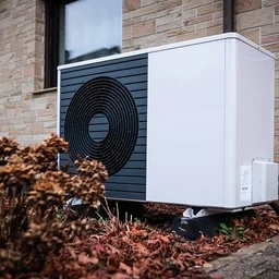 Air source heat pump unit outside a home surrounded by autumn leaves