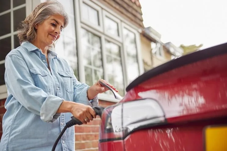 Mature Woman Attaching Charging Cable To Electric Car At Home